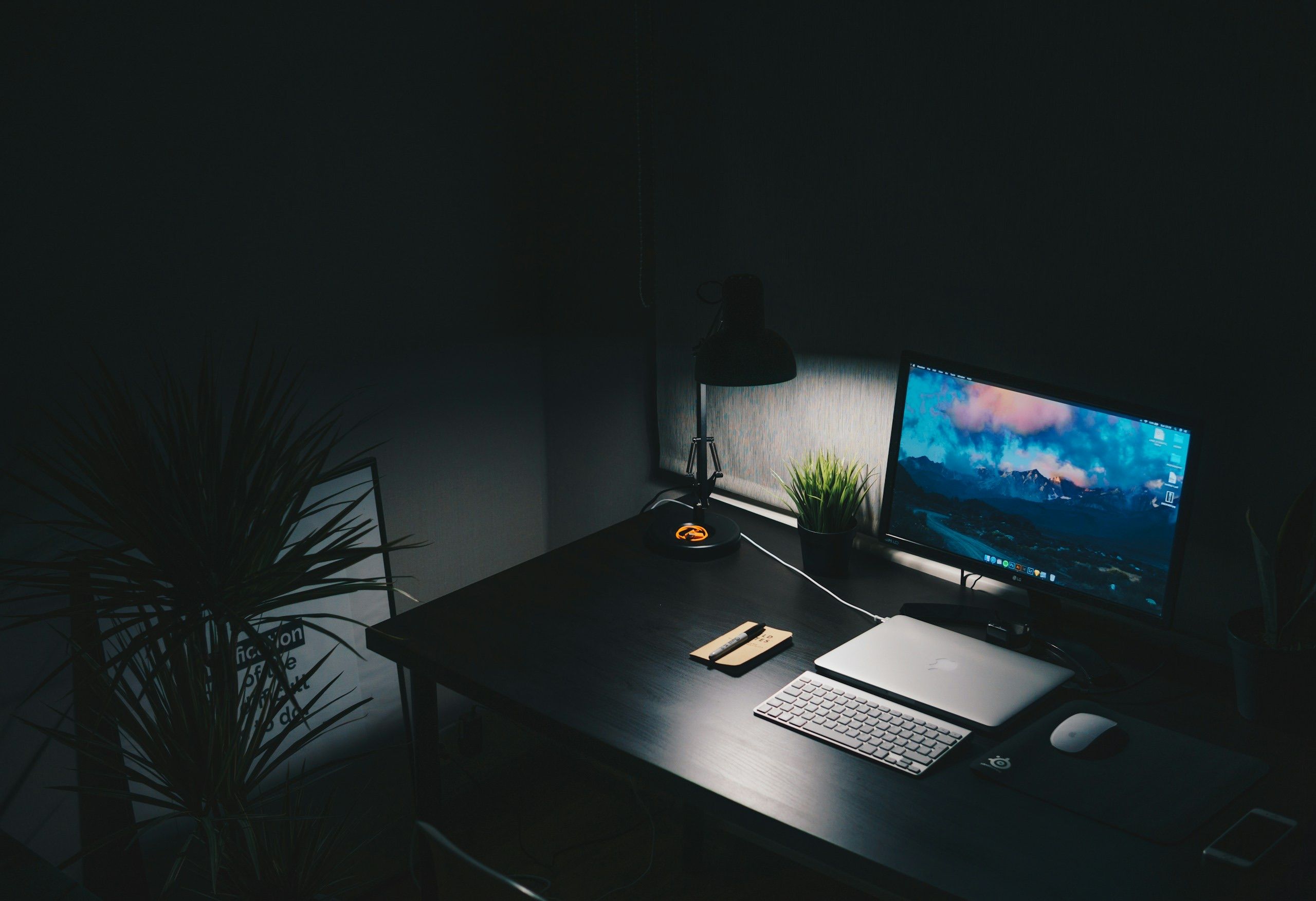 Dark developer desk with glowing monitor displaying terminal interface, illuminated by screen glow in an unlit room