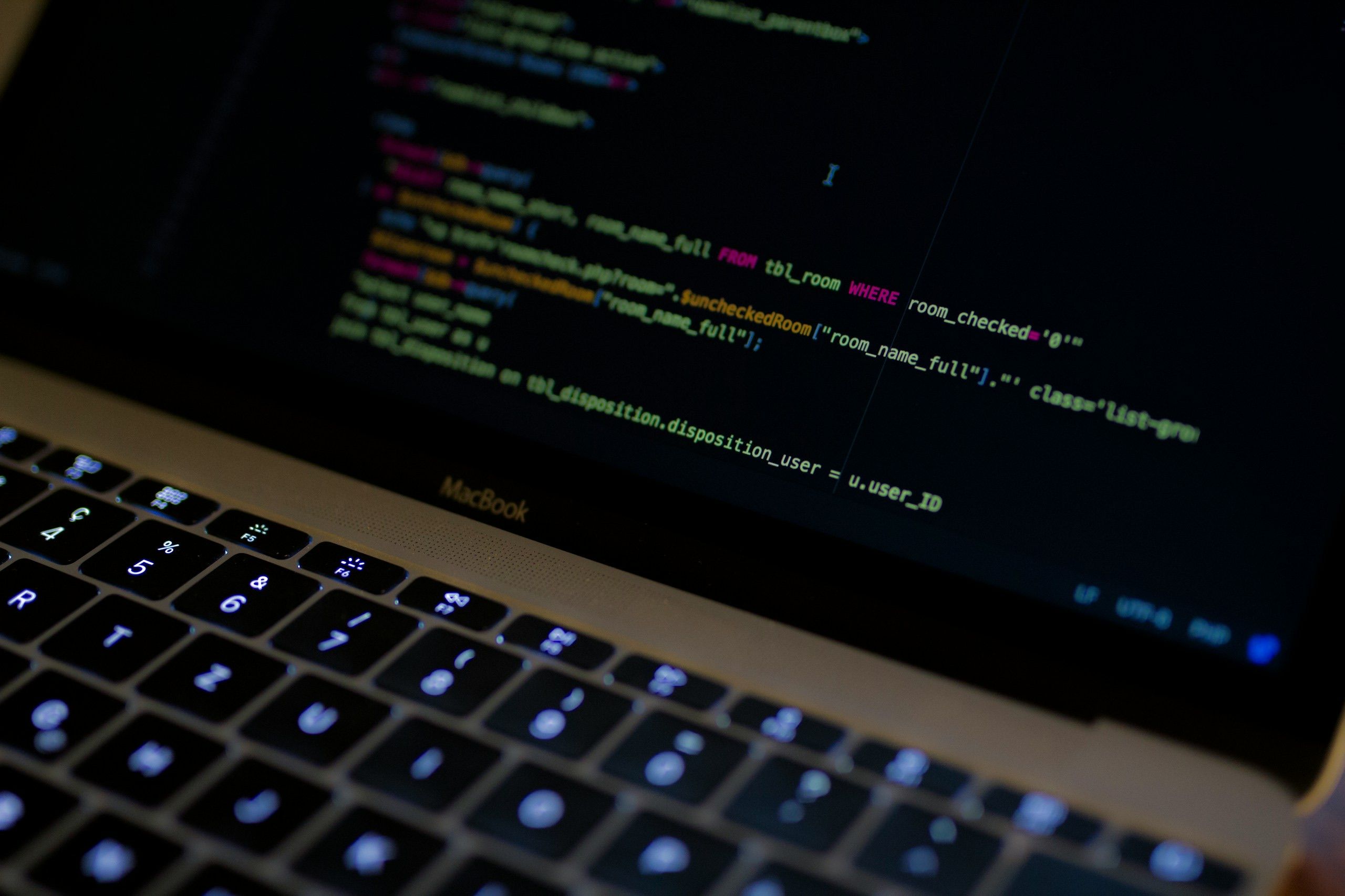 MacBook Pro displaying lines of Python code in a dark environment, lit only by the screen